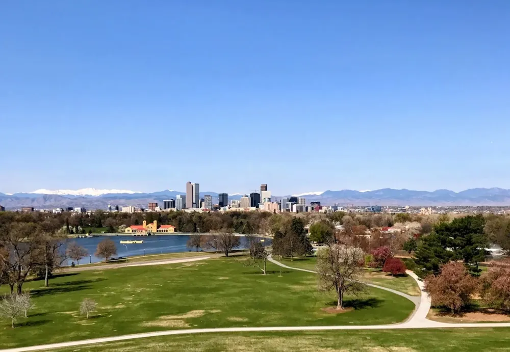 Ferril Lake and the Denver skyline seen across the lawns of City Park, with the snowcapped Front Range beyond