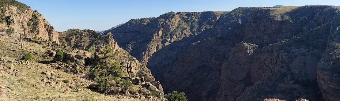 Grassy slope looking across a steep rocky canyon under a clear blue sky