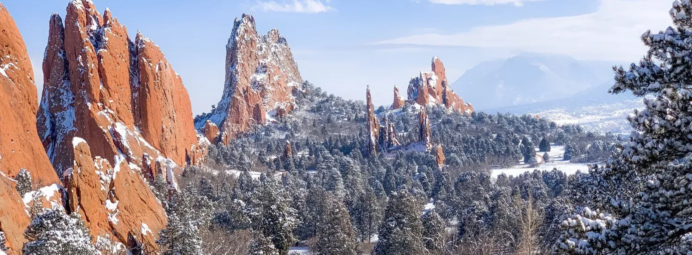Red sandstone formations at Garden of the Gods dusted with fresh snow, snowy pines below