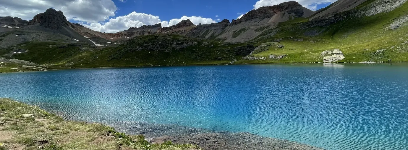 Turquoise Ice Lake ringed by rugged San Juan peaks under billowing clouds