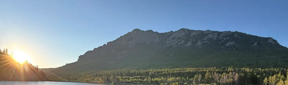 Sun rising over Lily Lake with a boardwalk trail along the shore and a mountain behind
