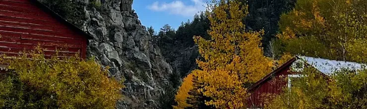 Red barn buildings beside a path at Golden Gate Canyon State Park, autumn trees and a rock outcrop