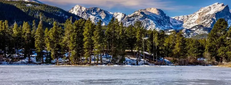 Frozen Sprague Lake edged with pines, snow-capped peaks of the Continental Divide behind