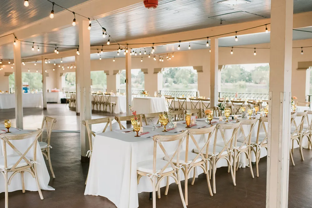 Reception tables set under the covered lakeside pavilion at Washington Park in Denver, string lights overhead and the water beyond